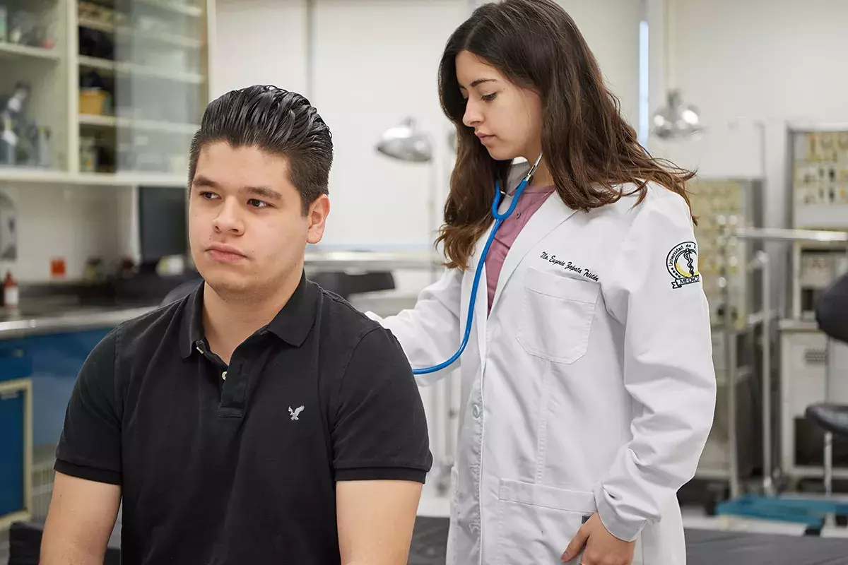 Alumna con estetoscopio revisando al paciente.