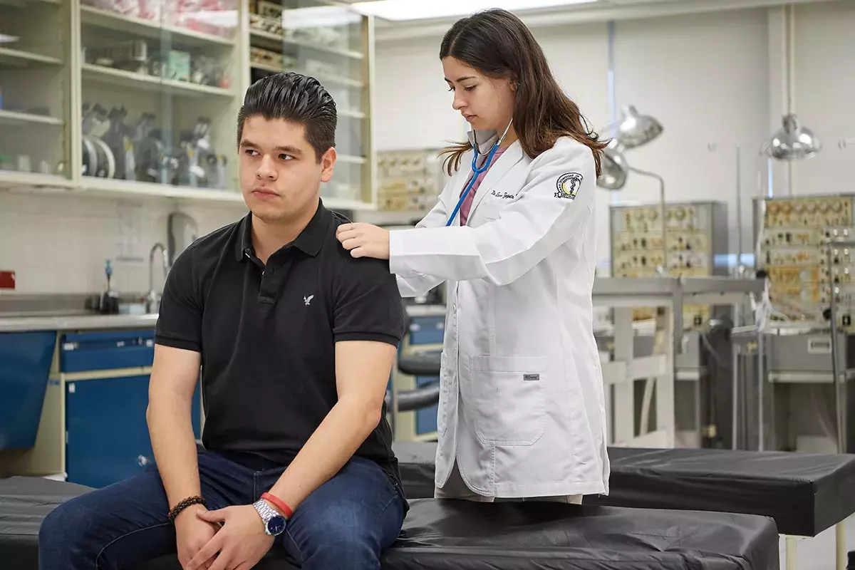 Alumna con estetoscopio revisando al paciente.