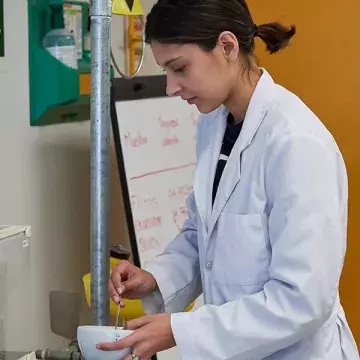 Alumna moliendo alimento en recipiente.