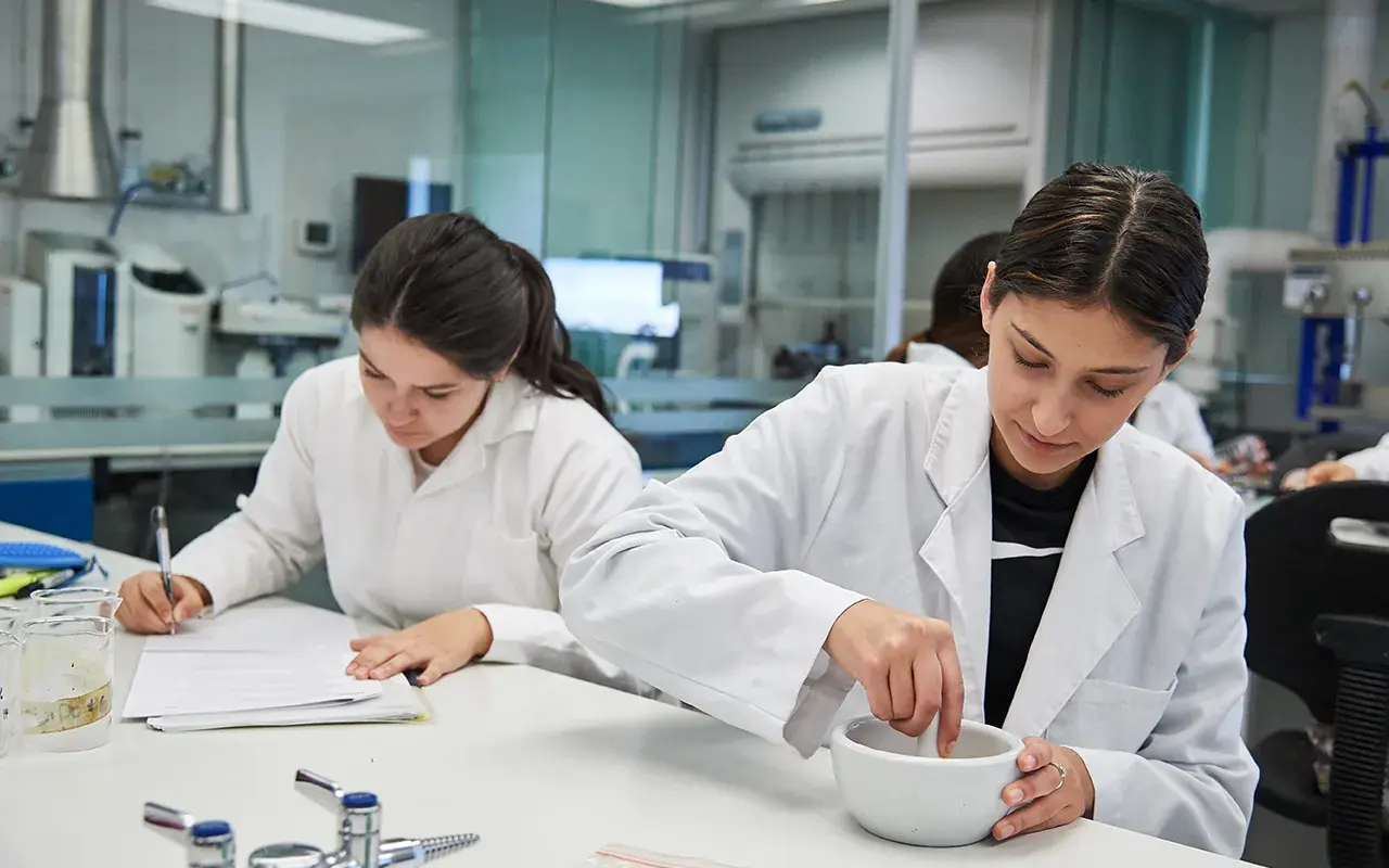 Alumna moliendo alimentos y alumna escribiendo.